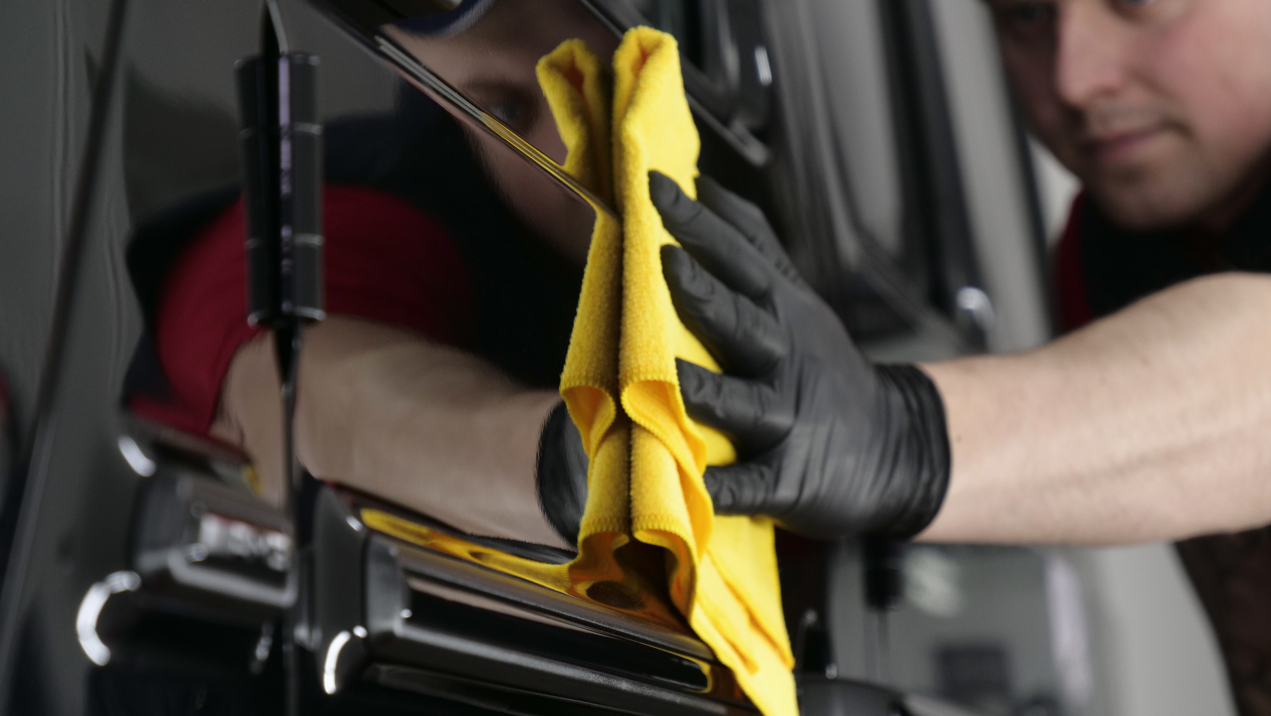 Person in black gloves drying a car window with a yellow microfiber cloth