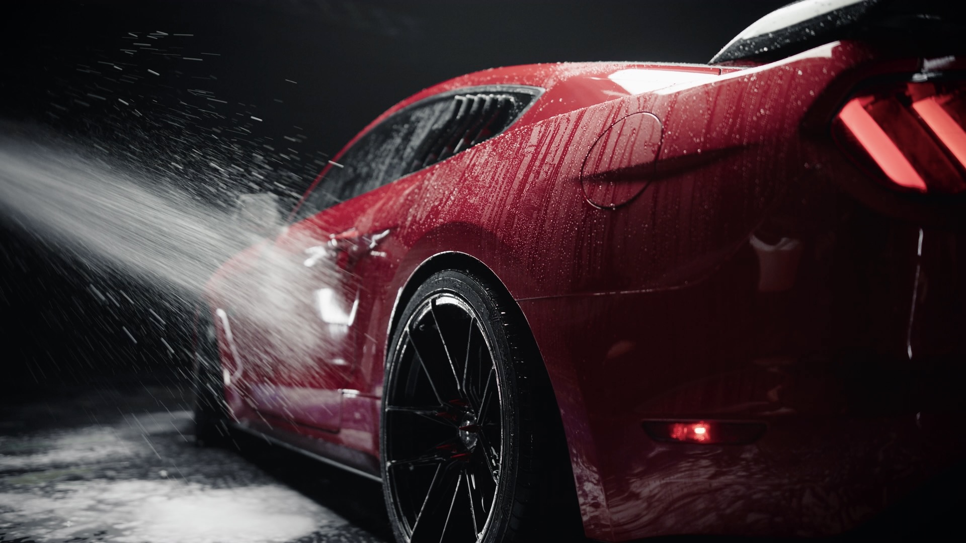 Red sports car being washed with high-pressure water stream against dark background
