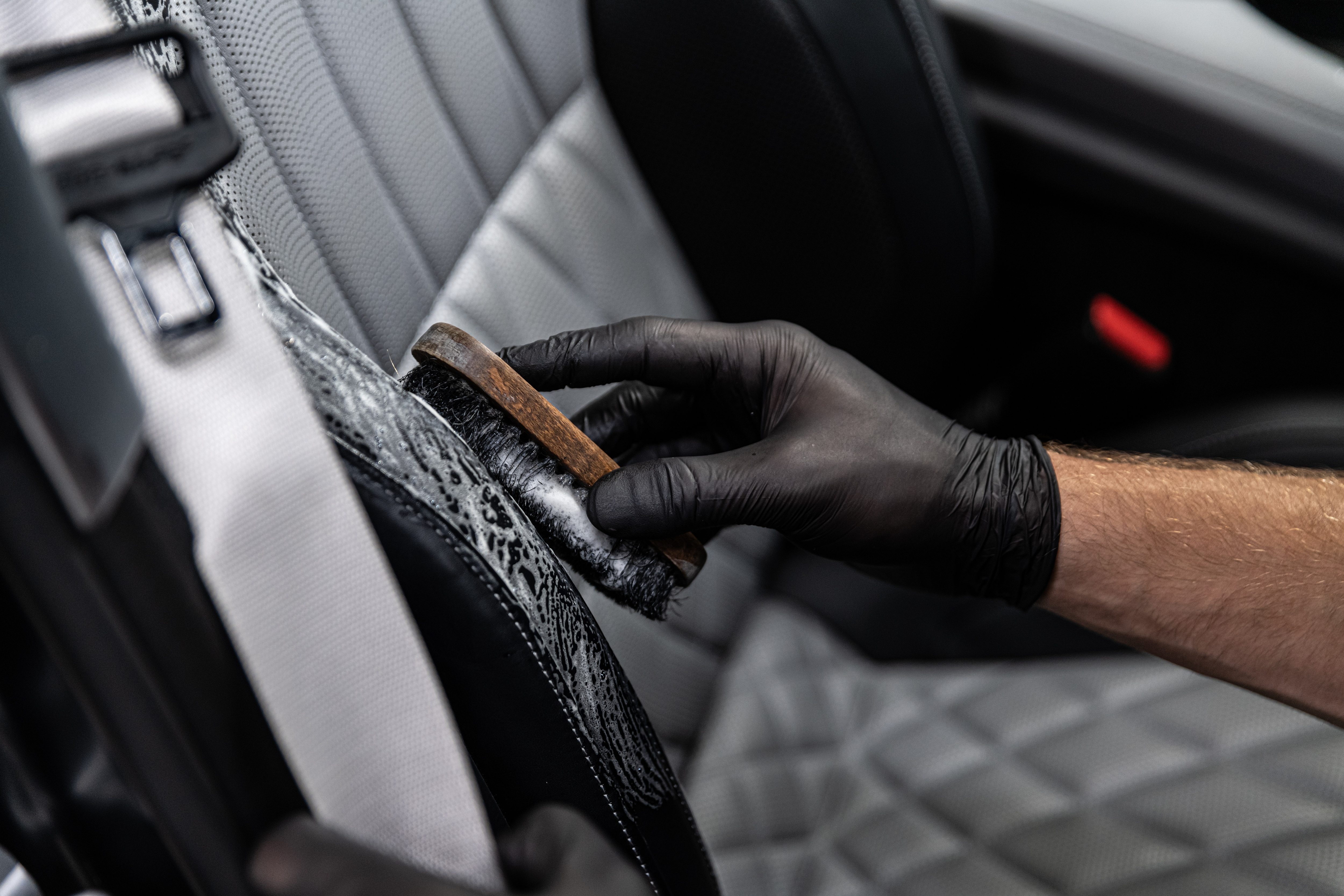 Professional detailing a car seat with brush and black gloves