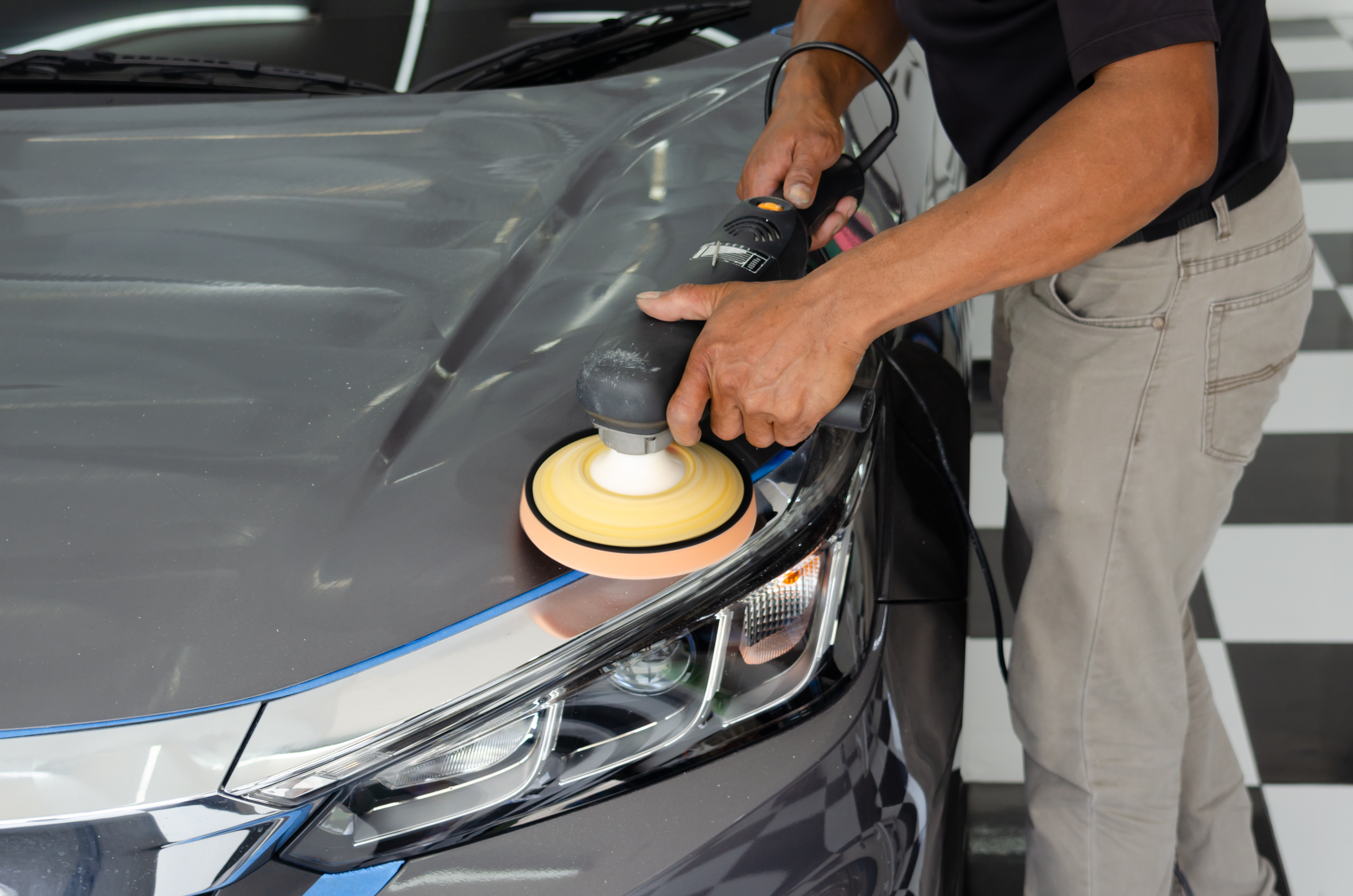 Professional detailer using orbital polisher with foam pad on gray vehicle hood